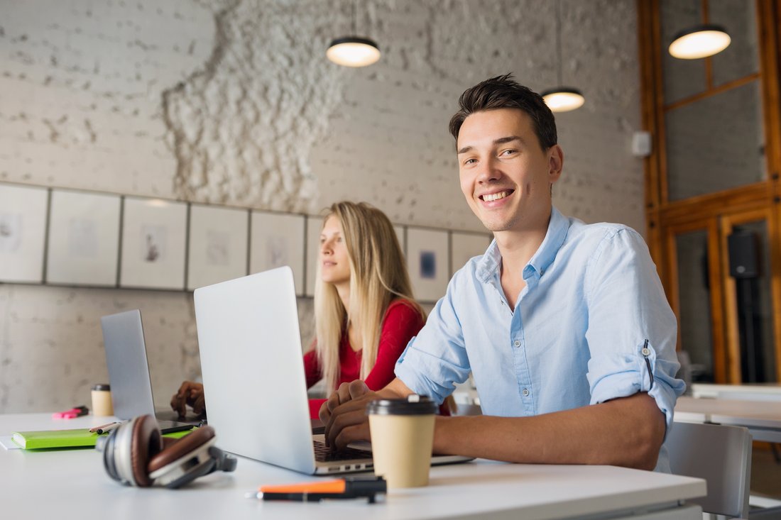 Uśmiechnięty młody mężczyzna przy laptopie w coworkingu