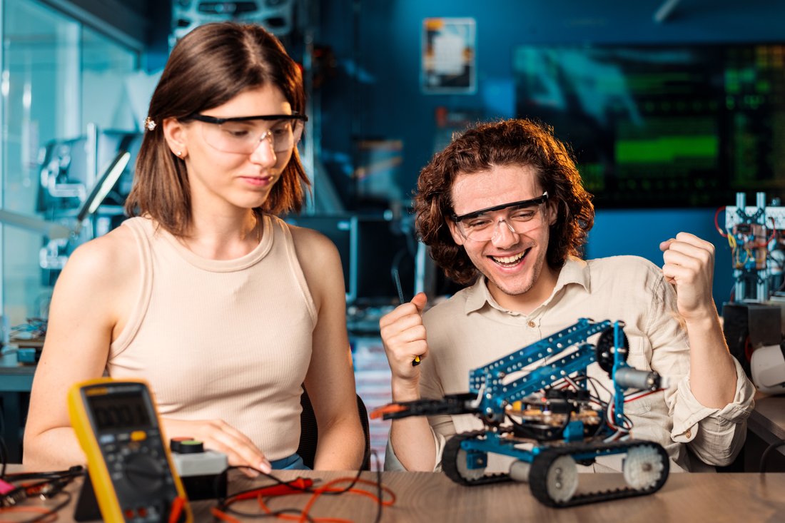 Studentka i student w okularach ochronnych budują robota w laboratorium