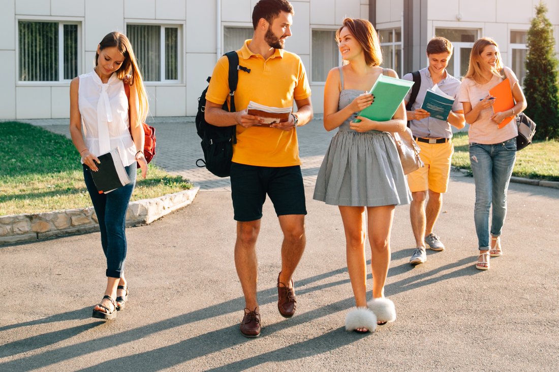 Studenci z notatkami idą razem przez kampus